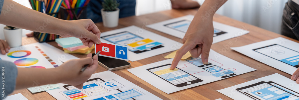 Poster Panorama shot of front-end developer team brainstorming UI and UX designs for mobile app on paper wireframe interface. User interface development team planning for user-friendly UI design. Scrutinize