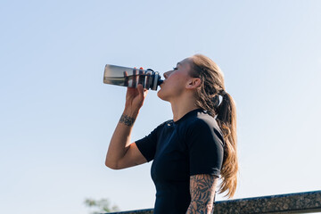 Fitness young sportswoman girl with tattoos doing sports in the morning drinking water while exercising outdoors in the city in the park health