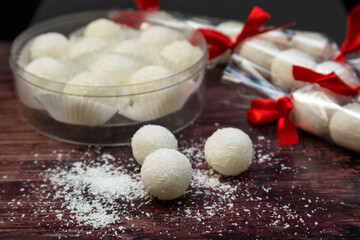 Round white candies with coconut flakes, in a gift box on a wooden background.