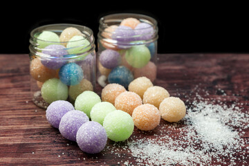 Colored round candy balls sprinkled with sugar in a glass jar and on a wooden table.