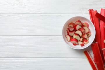 Rhubarb stalk and rhubarb pieces in bowl on white wooden background, space for text