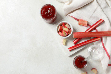 Rhubarb on white marble board, light towel and jars of jam on light background, space for text