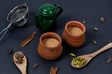 Fresh milk tea or indian karak chai or masala tea in clay cups with masala 
on dark background