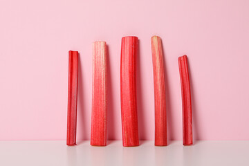 Five stalks of rhubarb stand on light pink background