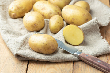 Whole potatoes and half of a tuber with a kitchen knife on burlap.