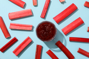 Jar of jam and pieces of rhubarb stalk on blue background, top view
