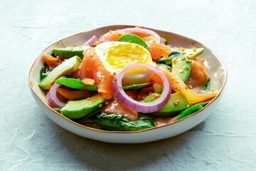 Salmon, avocado and egg salad with fresh leaves and onions, on a slate background. Healthy diet