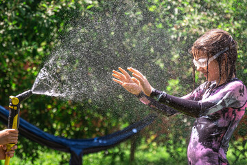 Funny little girl playing with garden hose in sunny backyard.