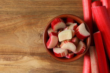 Sliced stalk of rhubarb in bowl on wooden background, space for tex