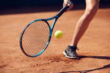 Cropped image of female legs in sportswear and tennis racket with ball over floor background with...