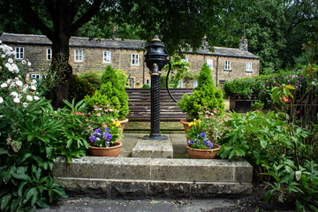 An old water pump has been used as the feature of a seat and garden in front of a terrace of stone cottages in Esholt in Yorkshire which was the setting for the TV soap opera Emmerdale
