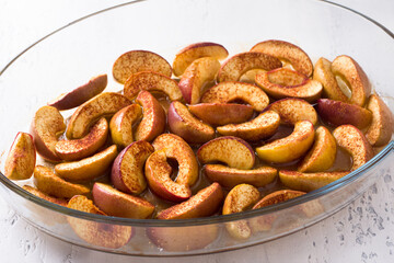 Baked apple slices with cinnamon, honey and lemon in a glass baking dish on a light blue background. Delicious homemade vegan dessert, cooking