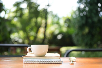 White coffee cup on wooden table with notebooks ]ans spoon on wooden table