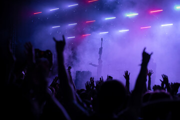 A group of people enjoy an illuminated music festival with raised arms. Concert Crowd in front of bright blue stage lights