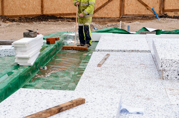 Builder placing polystyrene insulation boards on waterproofing membrane during floor construction. Energy saving concept - obrazy, fototapety, plakaty