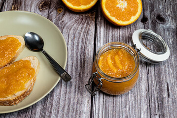 Delicious homemade orange marmalade in a glass jar. Top view of plate with slices of with homemade jam on white wooden table.