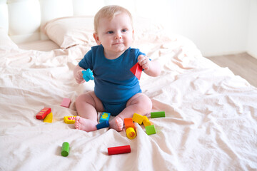 baby boy in blue bodysuit playing with colorful wooden eco toys on bed