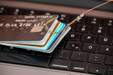 Visualisation of phishing and online fraud by a phished credit card on a PC keyboard hanging on a fishhook