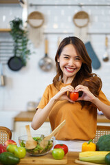 Happy Asian woman is eager to cook healthy vegetarian food and holds an appetizing tomato in her hand.