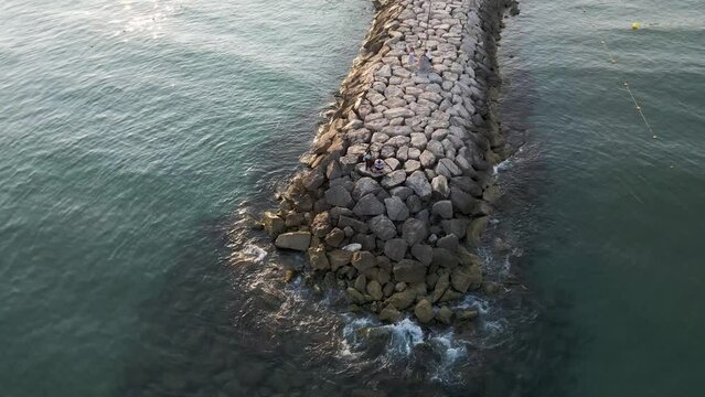 Aerial view of people on the breakwater at sunset along the Mediterranean Sea coastline, Sitges, Barcelona, Spain.