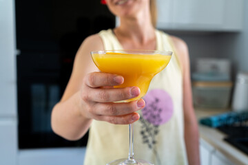 Woman holding an orange cocktail drink in a margarita glass.