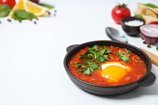 Shakshuka, spoon, slices of bread, tomato, lemon, basil, onion and spices on white background, space for text