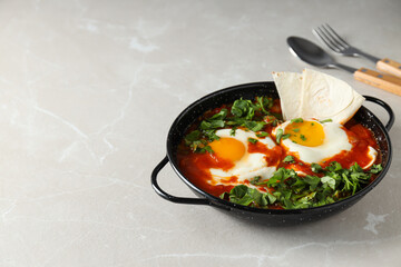 Shakshuka and pita in pan, spoon and fork on light background, space for text