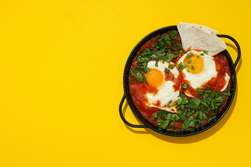 Shakshuka in pan and pita on yellow background, space for text
