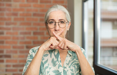 senior pretty woman looking serious and displeased with both fingers crossed up front in rejection,...