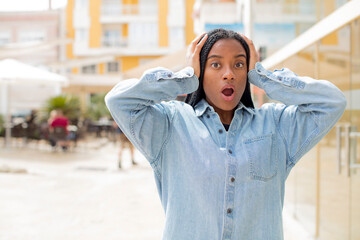 Fototapeta premium afro pretty black woman looking excited and surprised, open-mouthed with both hands on head, feeling like a lucky winner