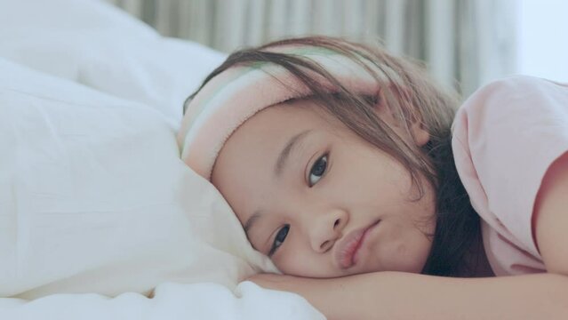 Face close up of adorable asian girl who is sleeping alone in her bed and white blanket with bright light shows concept of boring, stressfulness, unhappiness, tired emotion of child.