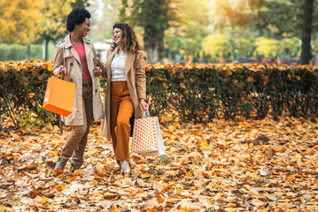 Happy woman friends walking in the forest in autumn with shopping bags.