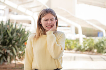 Fototapeta premium pretty young woman holding cheek and suffering painful toothache, feeling ill, miserable and unhappy, looking for a dentist