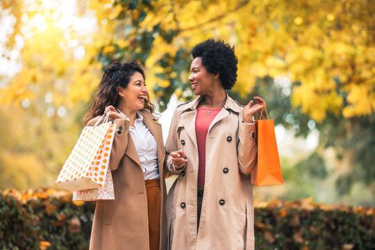 Happy woman friends walking in the forest in autumn with shopping bags.