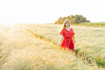 Young happy woman in red dress walking in wheat field on sunset. Breathe of freedom. Positive emotions feeling life, peace of mind. Mental health practice. Nature relaxation. Soft selective focus