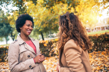 Happy woman friends walking in the forest in autumn. They are chatting and having fun.