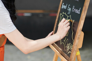 Closeup image of small business owner writing menu of street food cafe on chalkboard