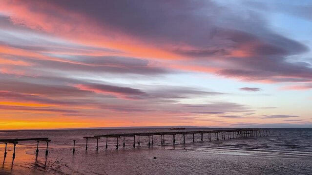 4K colourful view at sunrise of the old rotten pier with lenticular clouds moving along with calm waves in Punta Arenas, Patagonia, Chile