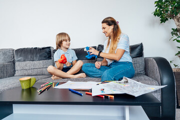 Happy mother and son playing role games with toys together in living room. Child psychotherapy...