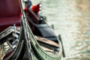 Fragment of a gondola, a Venetian boat on a blurred background of the canal water. Focus on the bow of the boat.