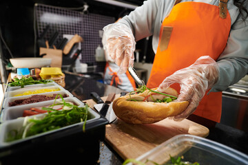 Gloved hands of cook putting greens in meat sandwich