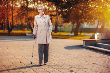 An older woman walking with a cane in the colorful park in the autumn