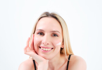 young blonde girl smiling with creams on her face leaning on her hand on white background