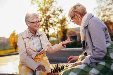Two older women playing chess in the colorful park in the autumn