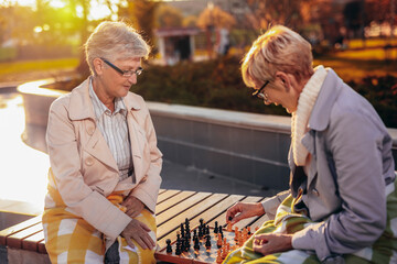 Two older women playing chess in the colorful park in the autumn