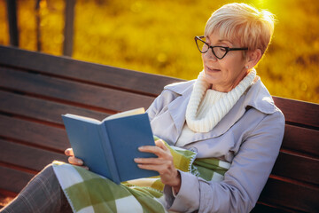 An older woman reading a book, sitting in the park, and enjoying the autumn