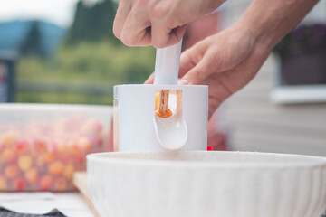 Worker uses a simple tool to extract pits from fresh cherries and prepare them for further use. Manual work with fruit. Seasonal work
