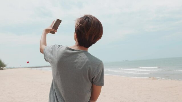 Cheerful Asian girl, she blends technology seamlessly with nature during her summer vacation. Using her smartphone, she connects with others, immersing in the beauty of sea and sky. 