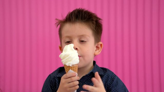 Niño rubio latino comiendo y disfrutando de un delicioso y rico helado para el calor en un fondo rosa en la heladería y paletería alegre y contento muy feliz saboreando una rica nieve en cono