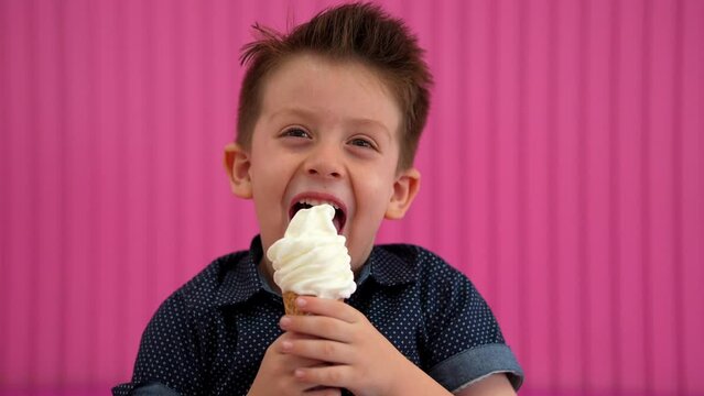 Niño comiendo y disfrutando de un delicioso y rico helado nieve para el calor en un fondo rosa en la heladería y paletería alegre y contento muy feliz saboreando